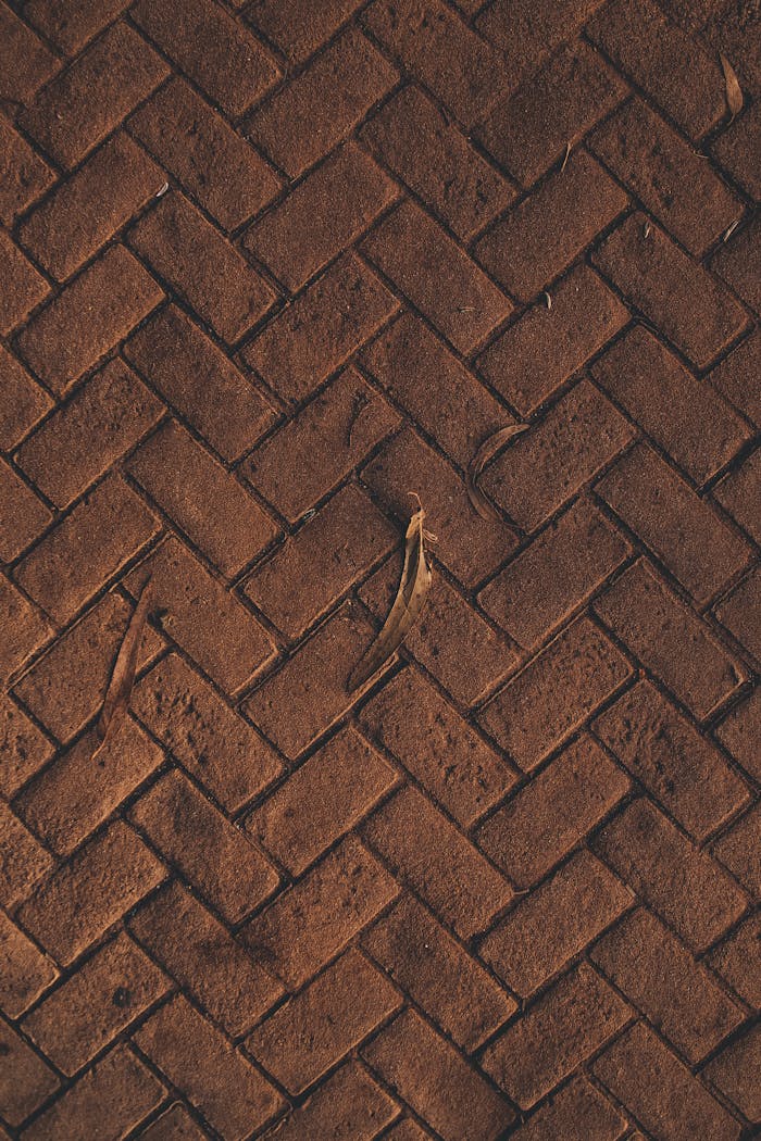 Close-up of a rustic brown herringbone brick pattern with rough texture and organic elements.