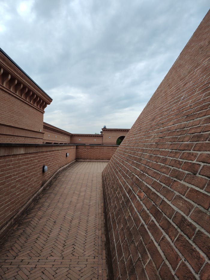 Low angle view of brick architecture and pathway under a cloudy sky, offering ample copyspace.