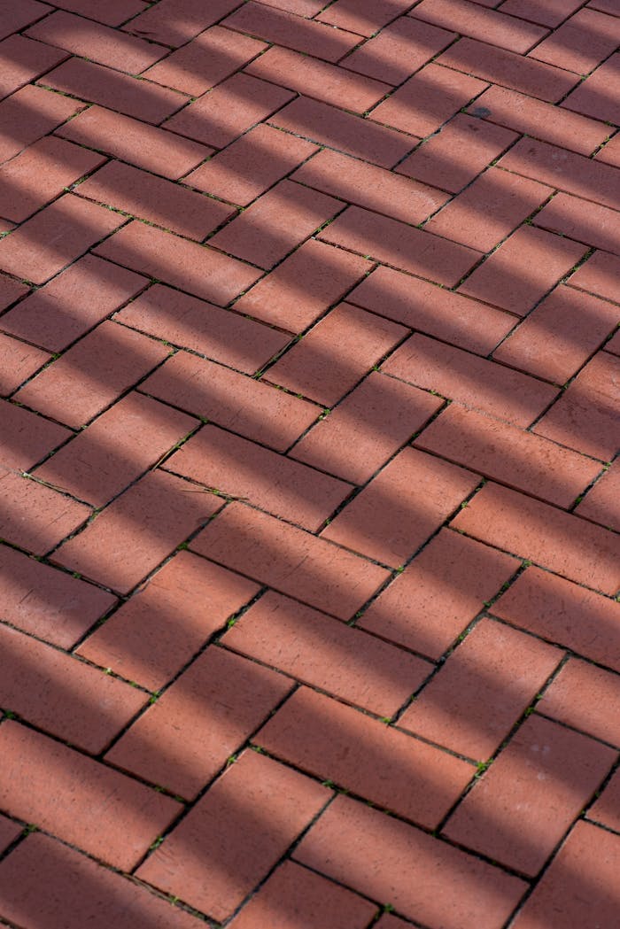 Close-up of textured red brick pavement with striking shadow patterns.